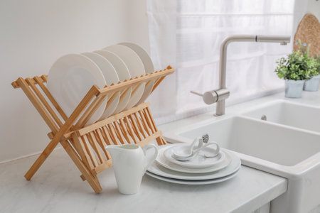 Drying rack with clean dishes on light marble countertop near sink in kitchenの写真素材