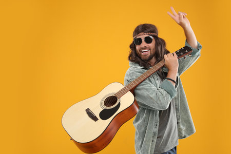 Stylish hippie man with guitar showing V-sign on orange background, space for textの写真素材