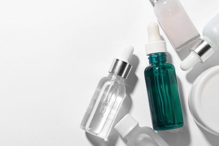 Many bottles of cosmetic serum on white background, flat lay. Space for textの写真素材