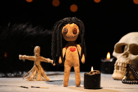 Female voodoo doll with pin in heart and ceremonial items on wooden table against blurred backgroundの写真素材