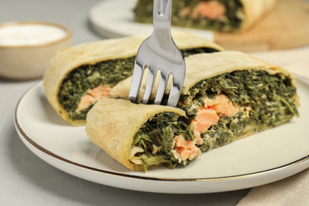 Eating delicious strudel with salmon and spinach at light gray table, closeupの写真素材