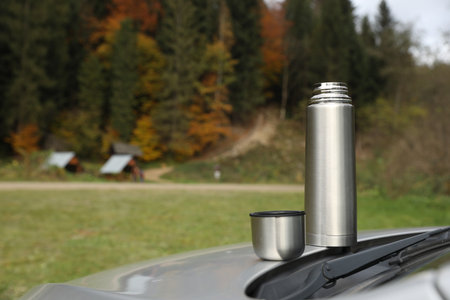 Metallic flask and cup lid on car trunk outdoors, space for textの写真素材
