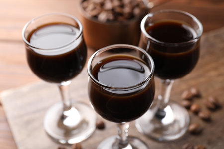 Shot glasses with coffee liqueur and beans on wooden table, closeup