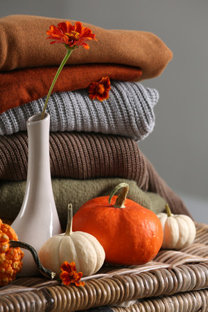 Beautiful autumn flowers, pumpkins and stacked clothes on wicker tableの写真素材