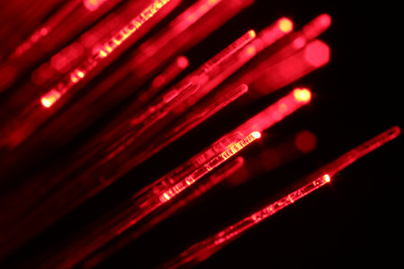 Optical fiber strands transmitting red light on black background, macro view