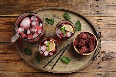 Delicious iced hibiscus tea, dry flowers, straws on wooden table, top viewの写真素材