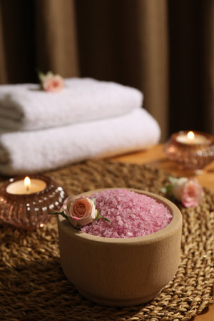 Bowl of pink sea salt, roses, burning candles and towels on wooden tableの写真素材