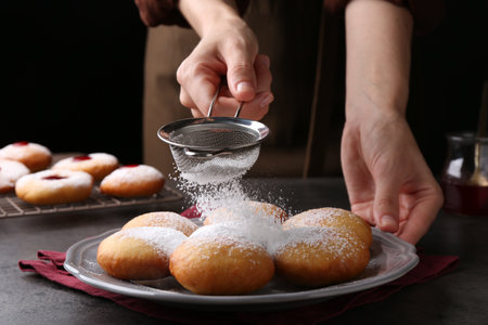 Woman dusting powdered sugar onto delicious Hanukkah donuts on gray table, closeupの写真素材