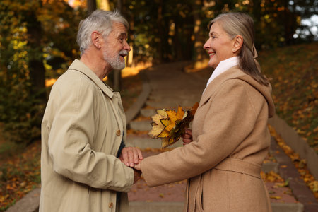 Affectionate senior couple with dry leaves in autumn park