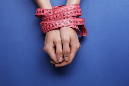 Woman tied with measuring tape on blue background, top view. Diet conceptの写真素材