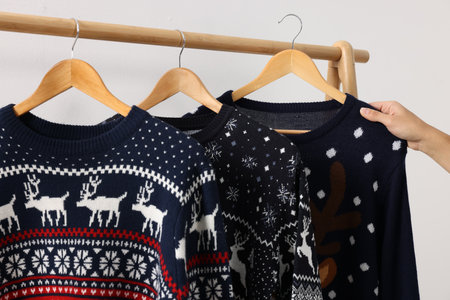 Woman picking Christmas sweater from rack near white wall, closeupの写真素材