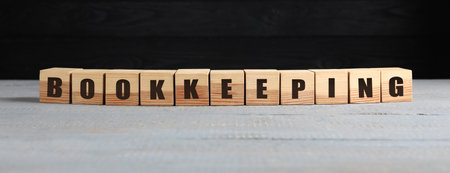 Word Bookkeeping made with cubes on light gray wooden table against black wall. Space for textの写真素材