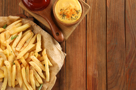 Delicious French fries served with sauces on wooden table, flat lay. Space for text