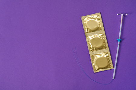 Contraception choice. Condoms and intrauterine device on purple background, flat lay. Space for text