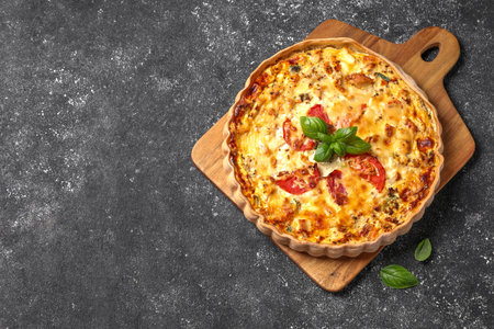 Tasty quiche with tomatoes, basil and cheese on dark textured table, top view. Space for text