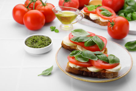 Delicious Caprese sandwiches with mozzarella, tomatoes, basil and pesto sauce on white table. Space for textの写真素材