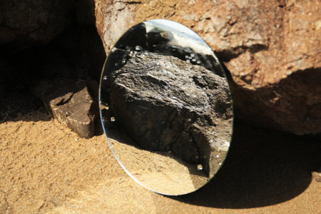 Round mirror reflecting seashore on sand near stones outdoorsの写真素材
