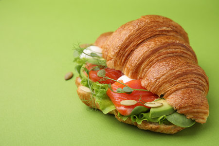 Tasty croissant with salmon, avocado, mozzarella and lettuce on green background, closeup. Space for textの写真素材