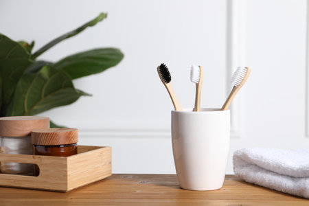 Bamboo toothbrushes in holder, towel, cosmetic products and leaves on wooden tableの写真素材