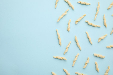 Uncooked trofie pasta on light blue background, flat lay. Space for textの写真素材