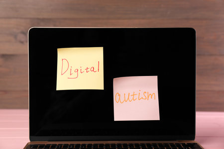 Sticky notes with phrase Digital Autism attached to laptop on table, closeup. Addictive behavior