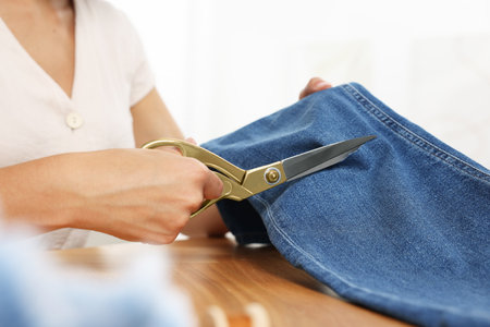 Woman cutting jeans with scissors at wooden table indoors, closeup