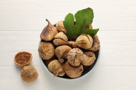 Bowl with tasty dried figs and green leaf on white wooden table, top viewの写真素材