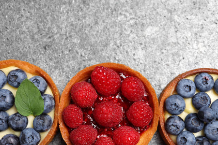 Tartlets with different fresh berries on light gray table, flat lay and space for text. Delicious dessertの写真素材
