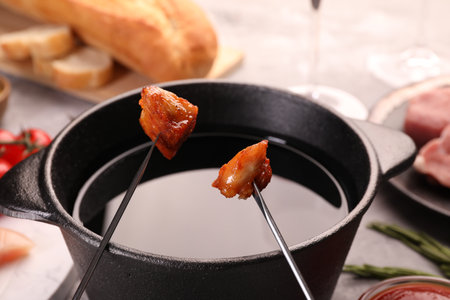 Fondue pot, forks with fried meat pieces and other products on gray table, closeupの写真素材