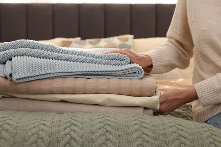 Woman with stack of different folded blankets on bed, closeup. Home textile