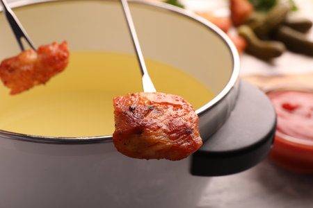 Fondue pot and forks with fried meat pieces on gray table, closeupの写真素材