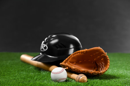 Baseball bat, batting helmet, leather glove and ball on green grass against dark backgroundの写真素材