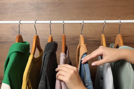 Woman choosing clothing with hangers near wooden wall, closeupの写真素材