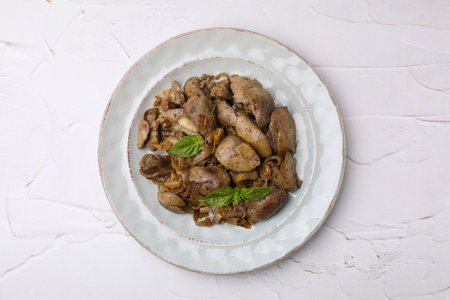 Plate of delicious fried chicken liver with onion and basil on white textured table, top viewの写真素材