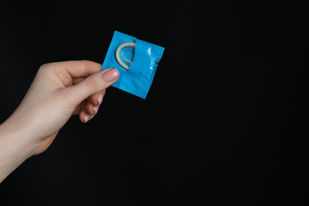 Woman holding condom on black background, closeup. Space for textの写真素材