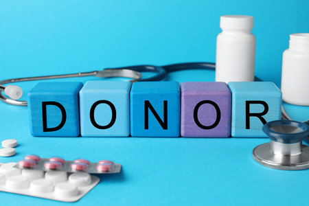 Word Donor made of wooden cubes, pills and stethoscope on light blue backgroundの写真素材