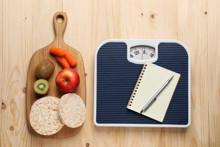 Healthy diet. Scale with notebook and products on wooden table, flat layの写真素材
