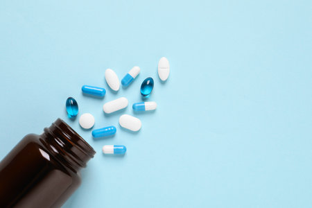 Plastic bottle with many different pills on light blue background, flat lay. Space for textの写真素材
