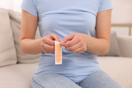 Woman opening sticking plaster on sofa indoors, closeupの写真素材