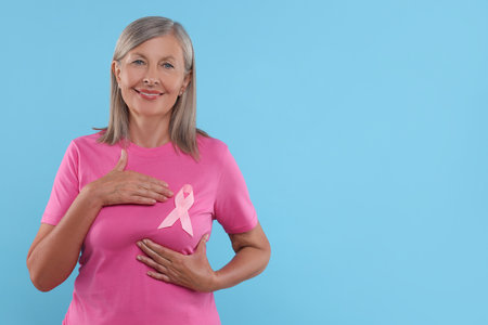Senior woman with pink ribbon on light blue background, space for text. Breast cancer awarenessの写真素材