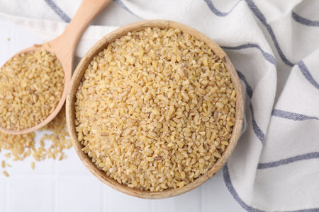 Bowl and spoon with raw bulgur on table, flat layの写真素材