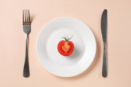 Plate with half of tomato and cutlery on beige background, flat lay. Diet conceptの写真素材