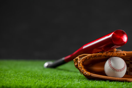 Baseball bat, leather glove and ball on green grass against dark background. Space for textの写真素材