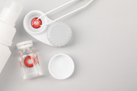 Case with red contact lenses, bottle of solution and tweeters on light gray background, flat lay. Space for textの写真素材