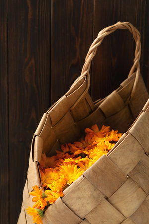 Beautiful calendula flowers in wicker bag against wooden wallの写真素材