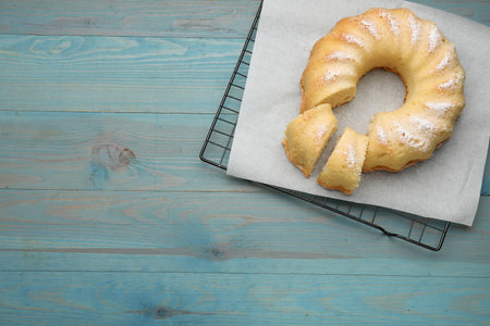 Delicious freshly baked sponge cake on light blue wooden table, top view. Space for text
