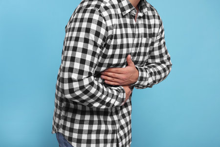 Man suffering from stomach pain on light blue background, closeupの写真素材