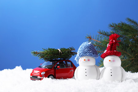 Cute decorative snowmen and toy car with fir tree branches on artificial snow against light blue background, space for textの写真素材