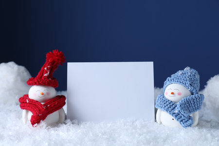 Cute decorative snowmen and blank card on snow against blue backgroundの写真素材