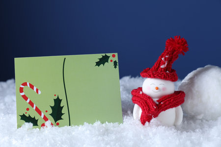 Cute decorative snowman and blank Christmas card on snow against blue backgroundの写真素材